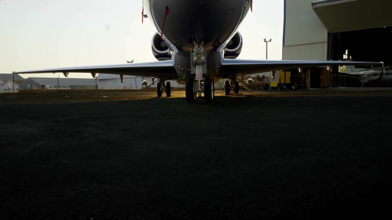 Jet privato parcheggiato su rampa asfaltata durante l'ora d'oro, con veicoli di supporto dell'hangar in design piatto.