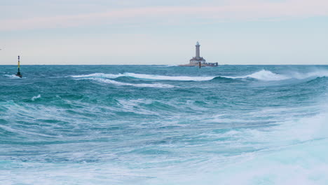 Stormy-big-sea-waves-creating-crest-on-lighthouse-Porer,-cardinal-mark-with-grebes-resting