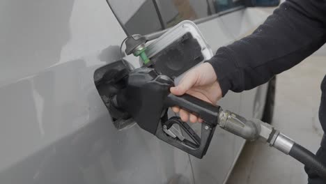 gasolinera hombre caucásico blanco con anillo de bodas llenando coche plateado insertando la boquilla de gas en el tanque y luego seleccionando el grado de combustible