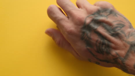 mano masculina tatuada dejando caer la píldora de suplemento de melena de león en la mesa amarilla