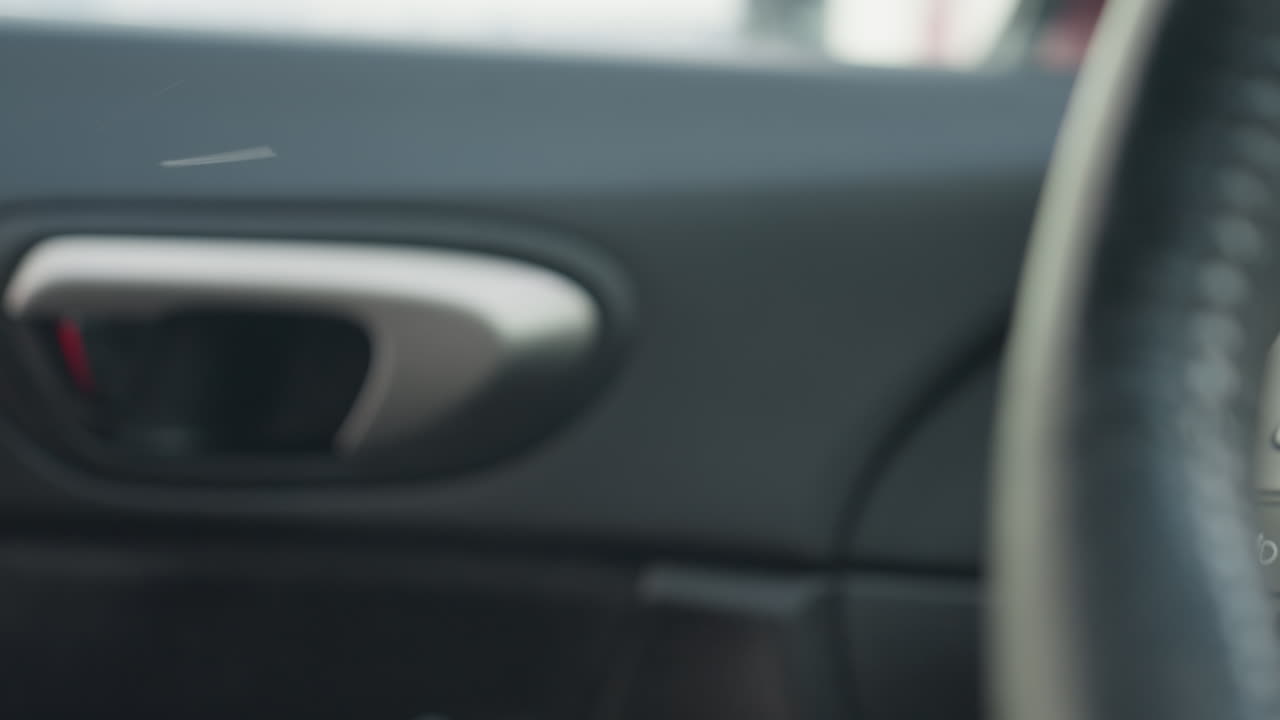 close up fair skinned hand reaches toward car interior door handle to open door as airborne particles float inside vehicle with steering wheel partially visible under soft natural lighting
