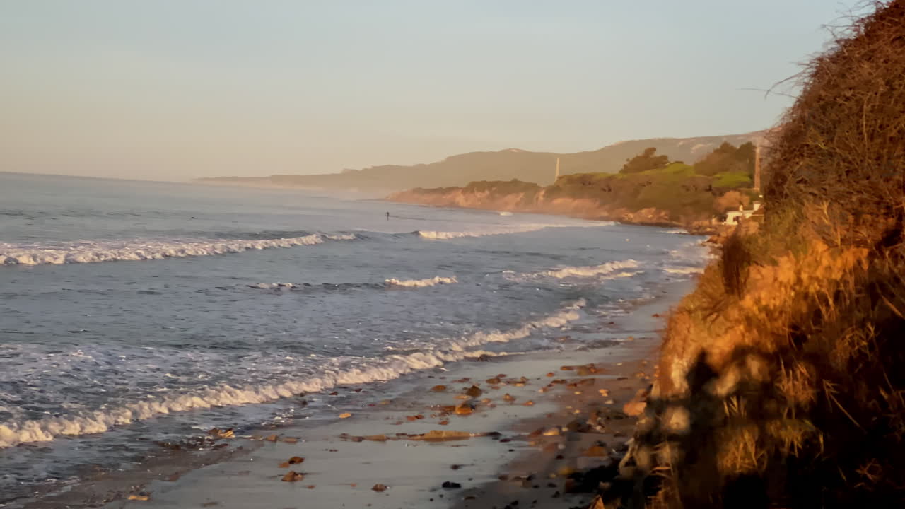 some Waves peel along the Hurricane Tarifa shoreline while a green hillside drops sharply into the sea at golden hour