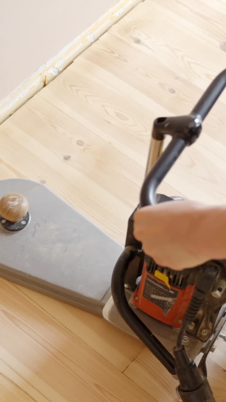 Sanding wood floor edges with a floor sander machine in a light-colored wooden room