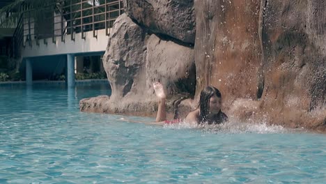 tanned lady in bright red bikini lies under blue waterfall