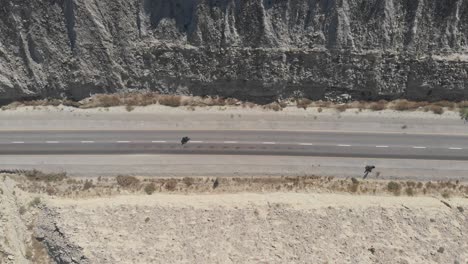 aerial birds eye view of motorbike driving along makran coastal highway road beside dramatic rock formations in hingol national park