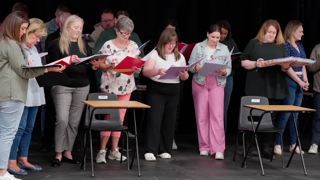 Panning right locked-off, talented theatre performers learning their lines