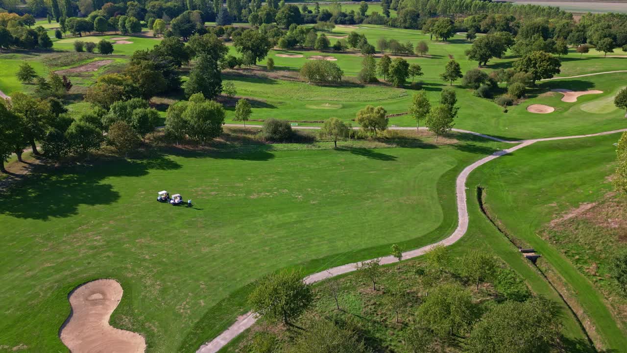 Large professional golf course with sand bunkers and curving pathways surrounded by greenery from above