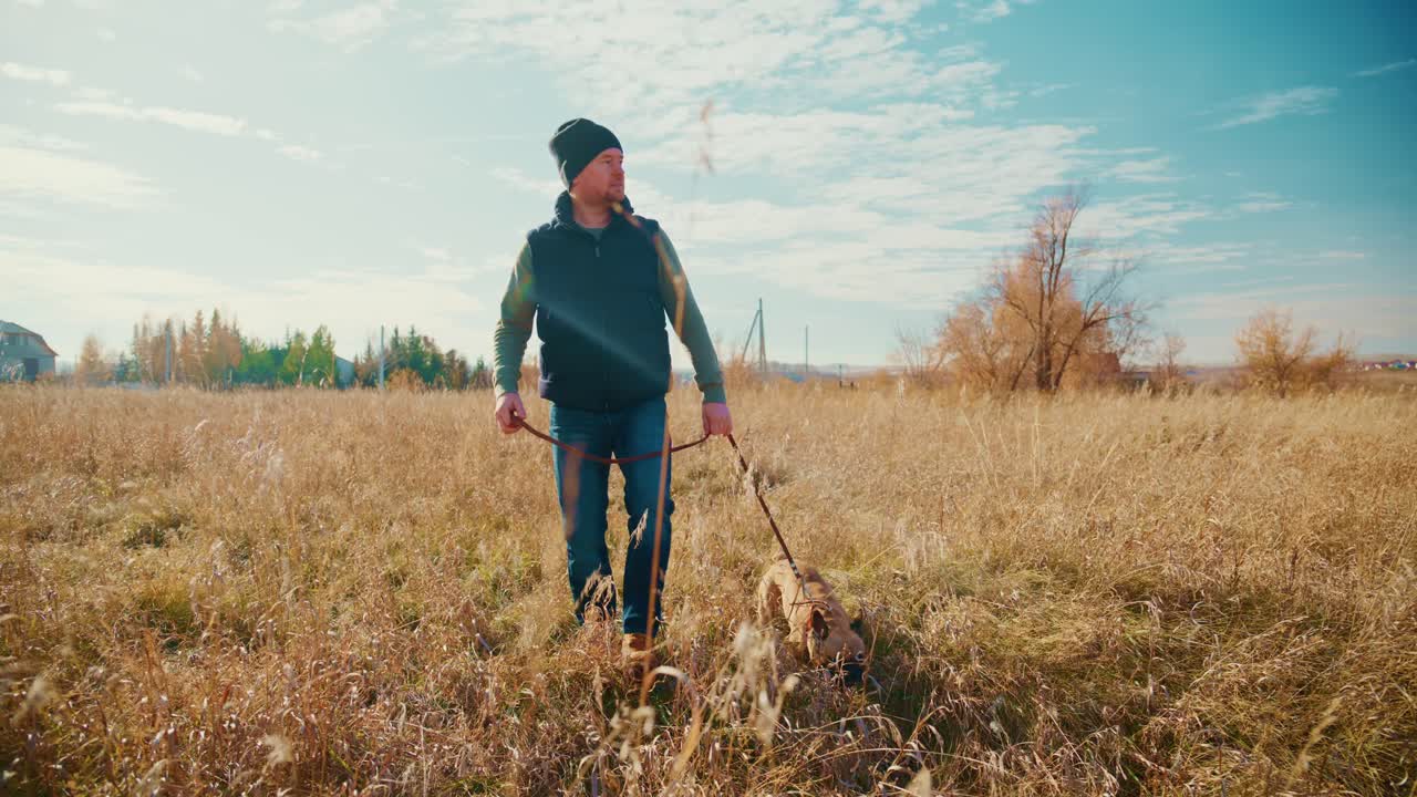 A man enjoys a serene walk with his playful dog through a golden, sunlit field, surrounded by nature's beauty, showcasing their bond and the tranquility of the outdoors in a picturesque landscape