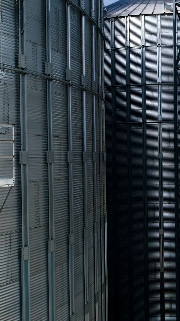 Large metal silo for storing grain. Modern industrial plant. Granary. Silver containers storing agriculture crop. Grain elevators on nature background. Close-up. Motion up. Vertical video