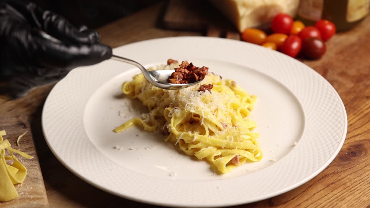 Chef che aggiunge pancetta croccante alla pasta Carbonara appena preparata