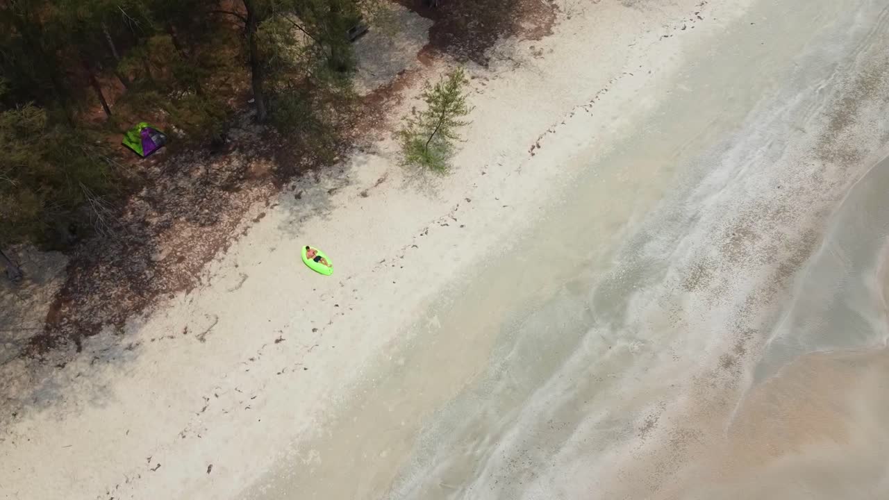 hombre acostado en el sofá de aire verde en la playa de arena con carpa detrás