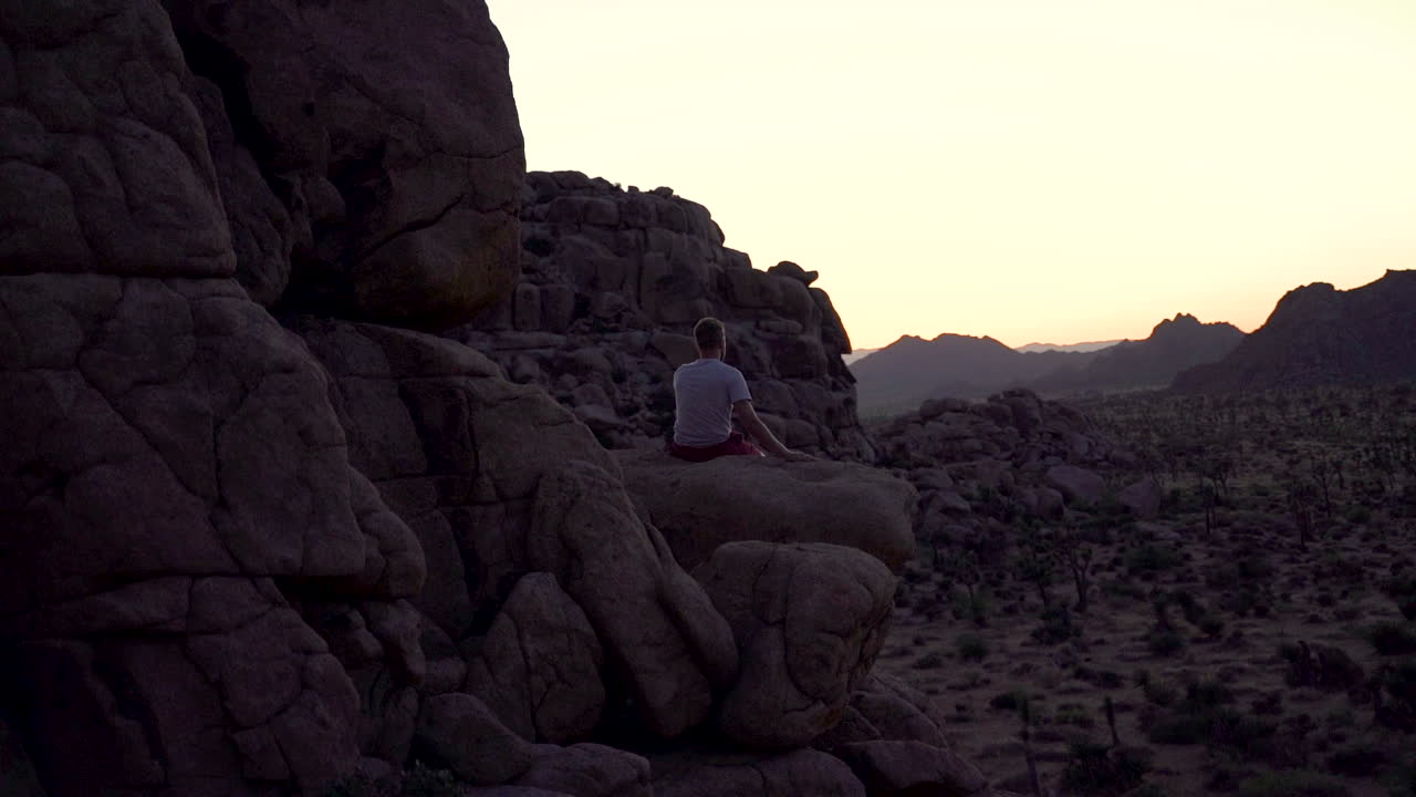 절벽 가장자리에 앉아 혼자 스카이라인을 바라보며 평화와 성공을 느끼는 남자의 실루엣