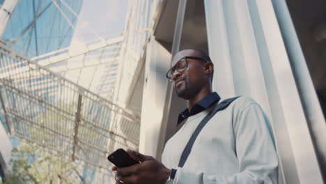 African-American-businessman-walking-through-city-using-smart-phone