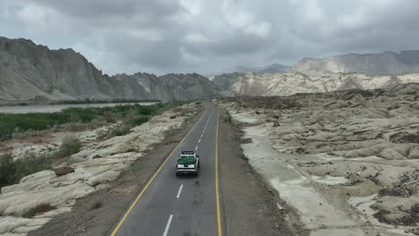 drone tracking a jeep car on the road driving towards beautiful landscape of mountain and hills hingol baluchistan