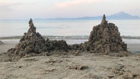 夕陽前面的兩座沙城堡的海灘景色,背景是慢動作中的水波