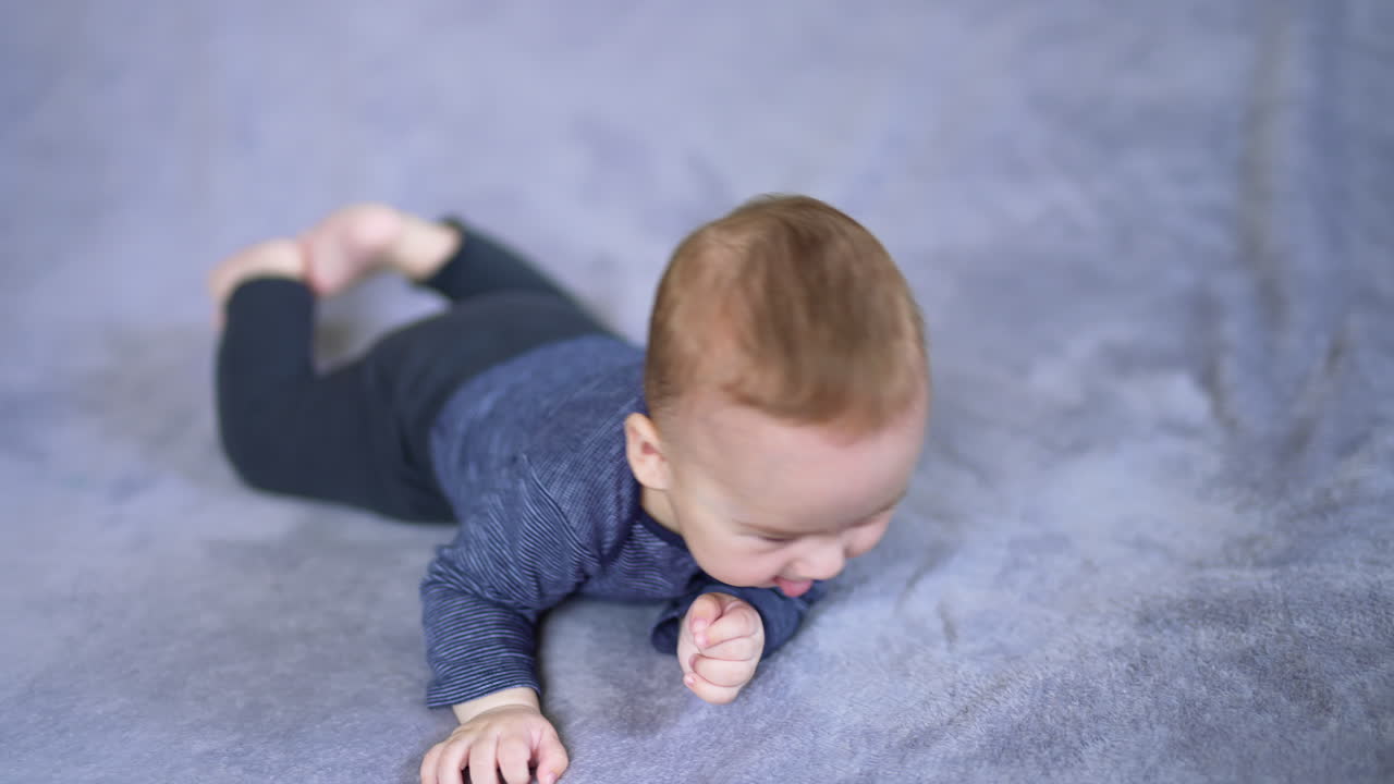 Cute healthy boy lies on a soft plaid. Little infant child turns around and looks up on the big bed. Blurred backdrop.