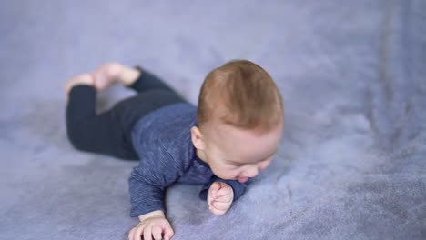 cute healthy boy lies on a soft plaid. little infant child turns around and looks up on the big bed. blurred backdrop.