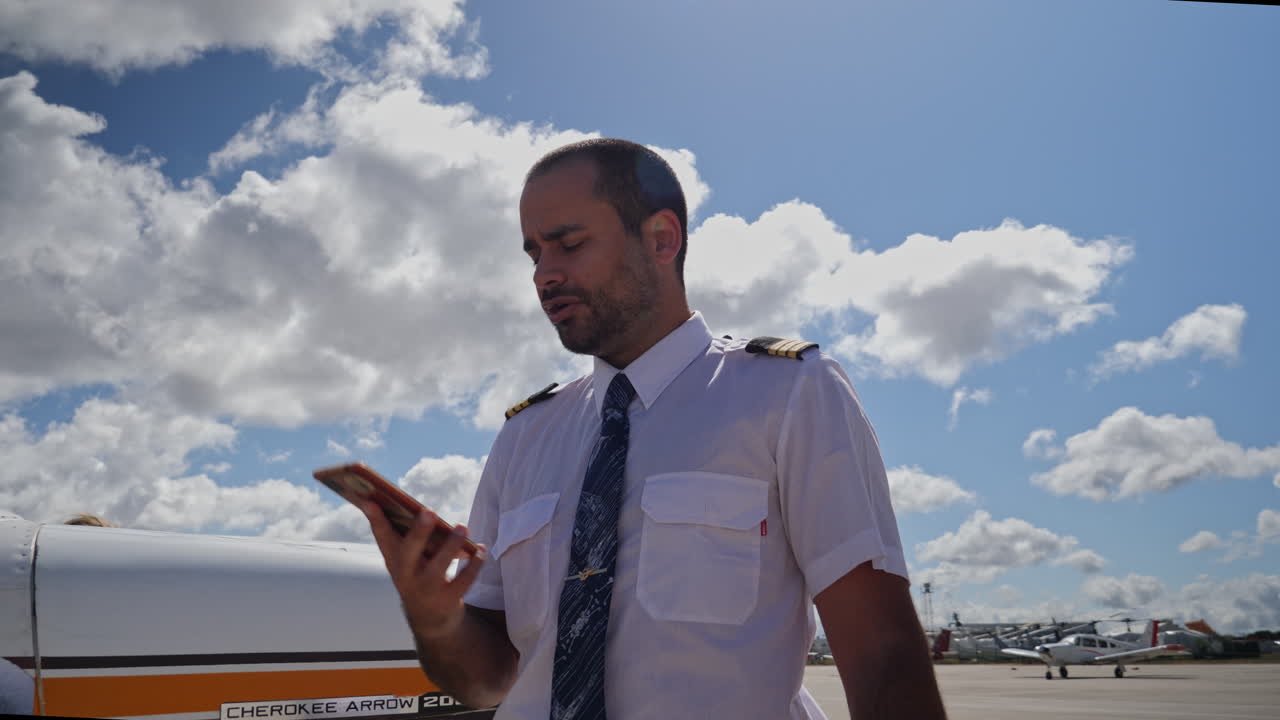 un piloto masculino habla por teléfono cerca de su avión en la zona de la plataforma