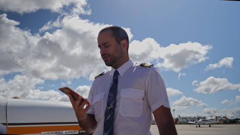 a male pilot speaks at phone near his plane on apron zone