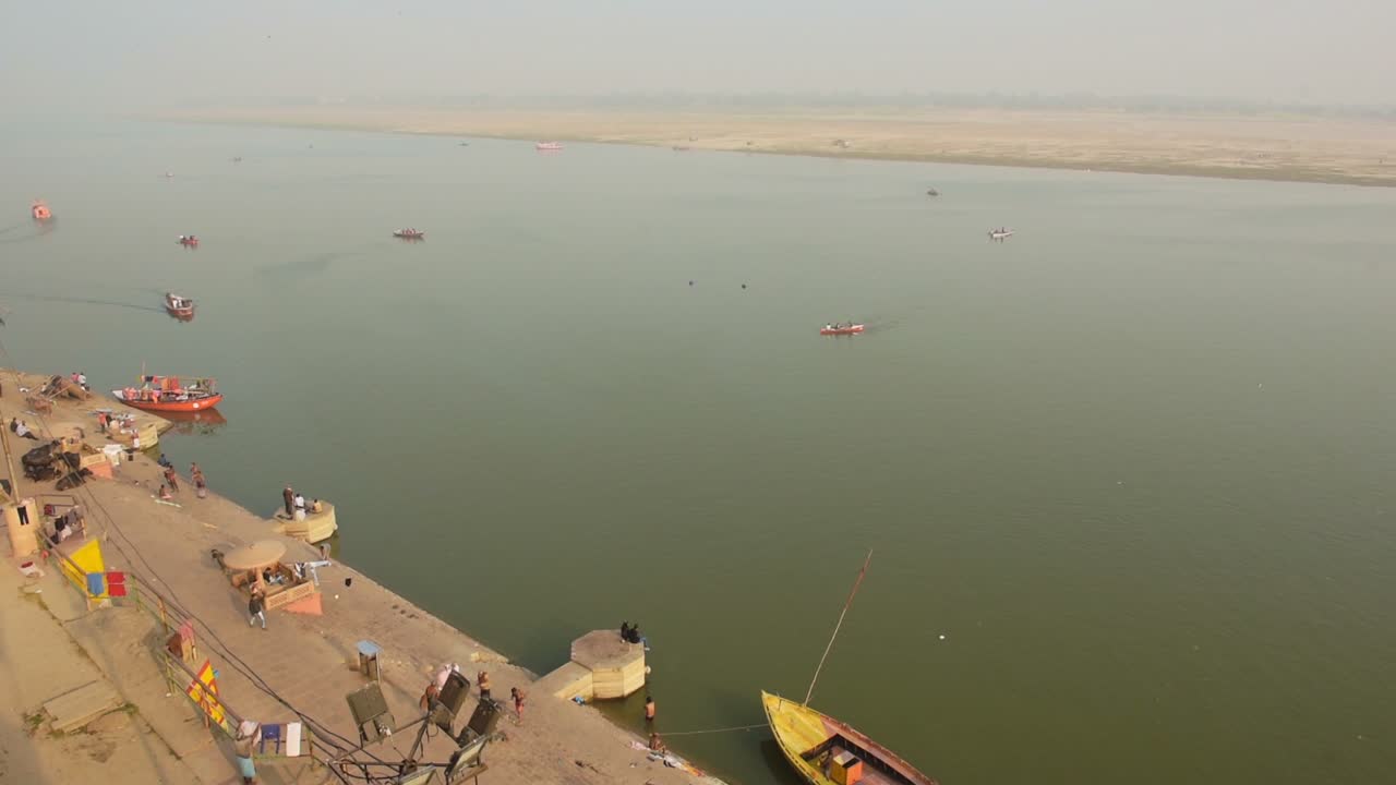 Indians Relaxing In The Coastline And The Boats Sailing Through The Ganges River. -wide shot