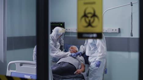 medical staff in full ppe attending to an elderly patient in an isolation ward