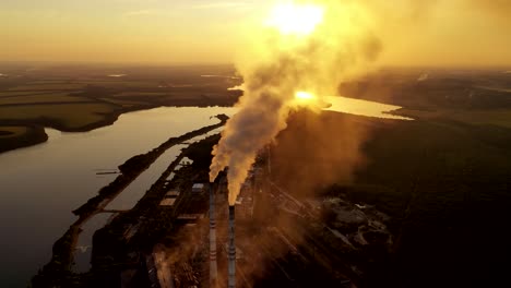 industrial plant near the river. metallurgical factory with large pipes. dirty emissions coming out of pipes into the air at sunset. aerial view.