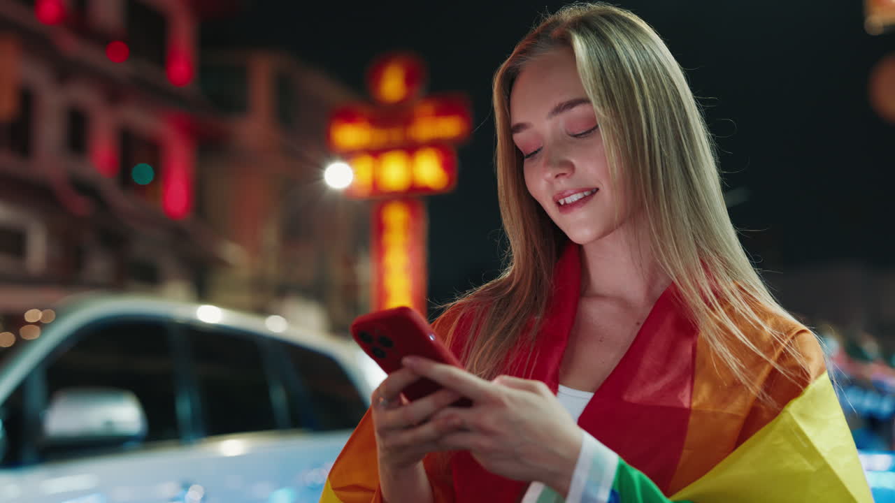 Young Woman Using Smartphone at Night in City with Pride Flag