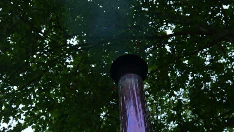 looking up at metallic flue with steam and heat being expelled under forest canopy