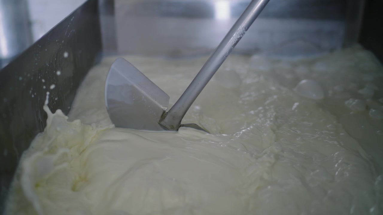 Milk churning in a large stainless steel vat at a dairy processing plant, ensuring quality and consistency