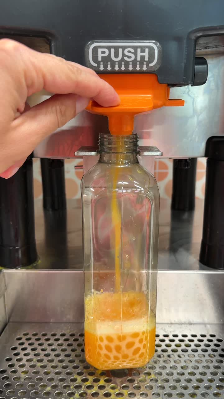 Person filling a plastic bottle with orange juice from a vending machine