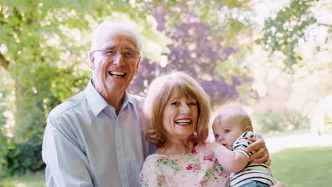 portrait of smiling senior couple outdoors with baby grandson