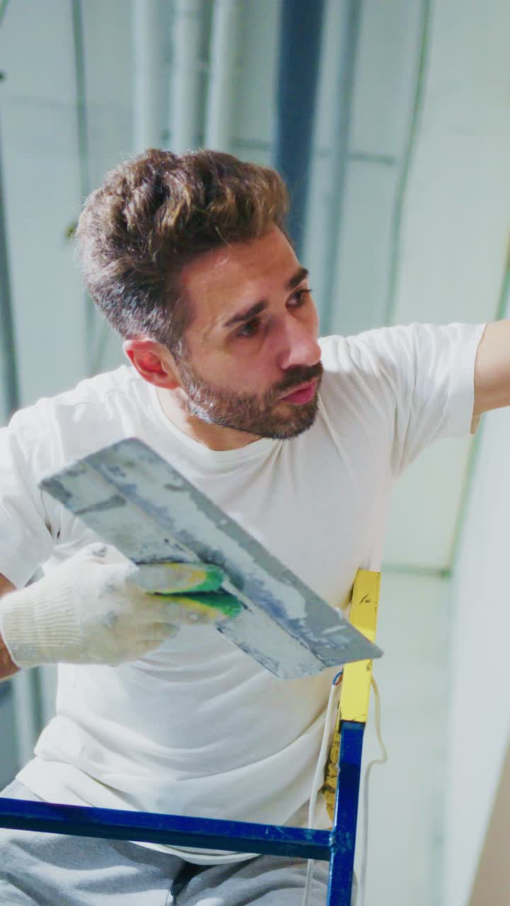 A dedicated worker focuses on painting a wall while perched on a ladder, demonstrating skill and precision in home improvement and renovation tasks