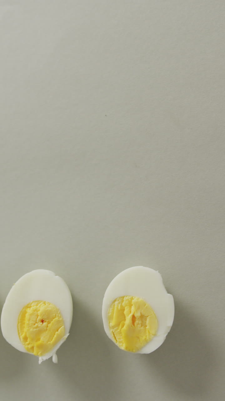 Vertical video of high angle view of two halves of hard boiled eggs with copy space on grey