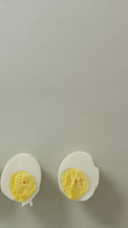 vertical video of high angle view of two halves of hard boiled eggs with copy space on grey