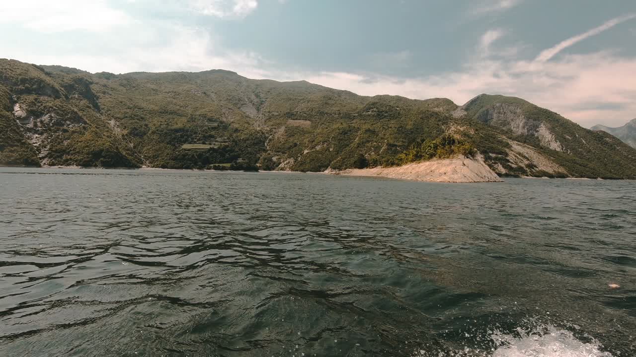 Sailing on vibrant water of lake surrounded by beautiful mountains with green vegetation on a cloudy day