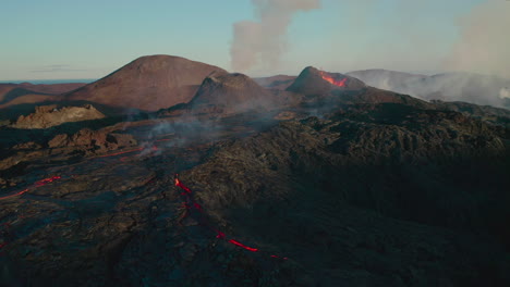 aerial flyover epic volcanic area with erupting volcano crater and flowing lava during blue sky and sunlight in iceland