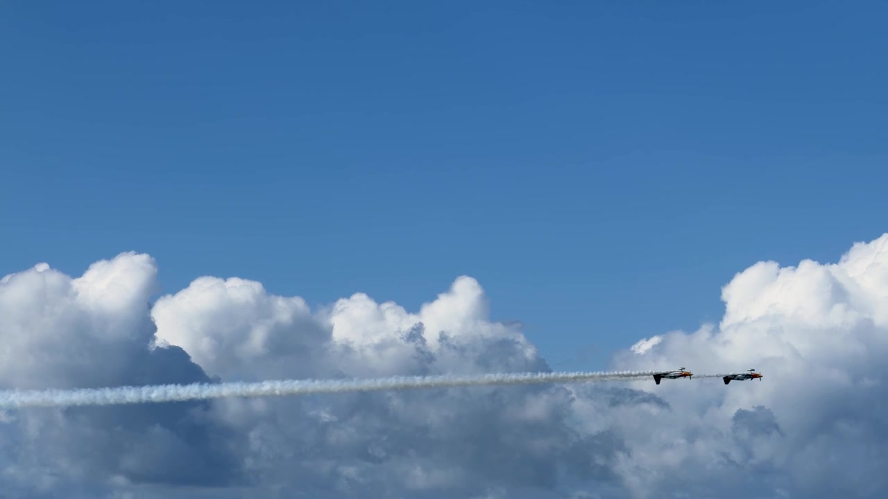 青い空と白い雲を背景に、スモークを出しながら水平に飛行する2機のスタント機