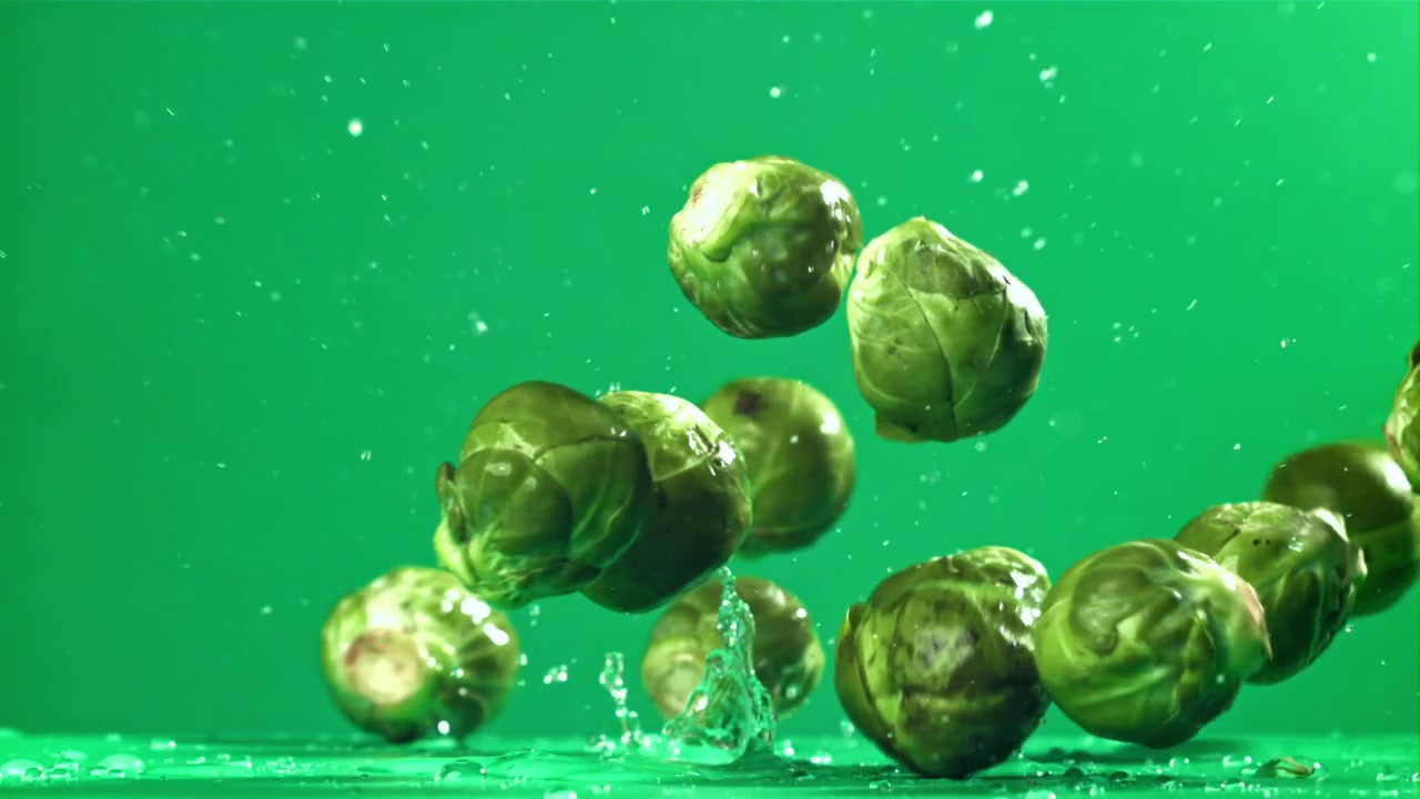 Cavolini di Bruxelles freschi che cadono e schizzano su sfondo verde
