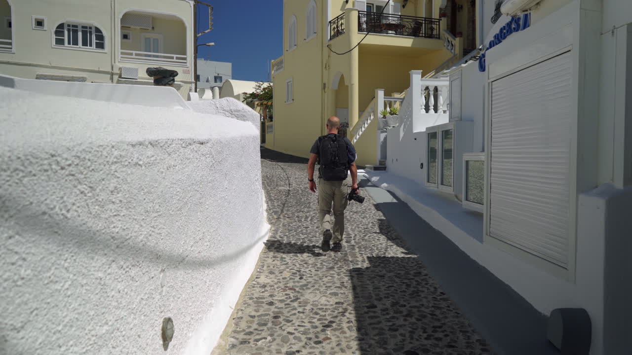 siguiendo a un hombre caminando por una calle estrecha en la isla de santorini