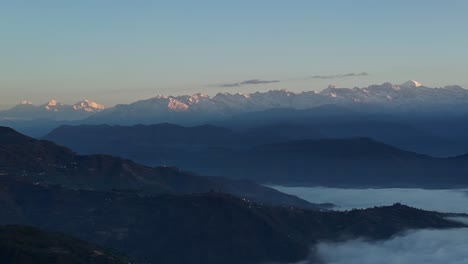 aerial pan across low clouds settled on nepalese valleys, mountain peak ridges behind