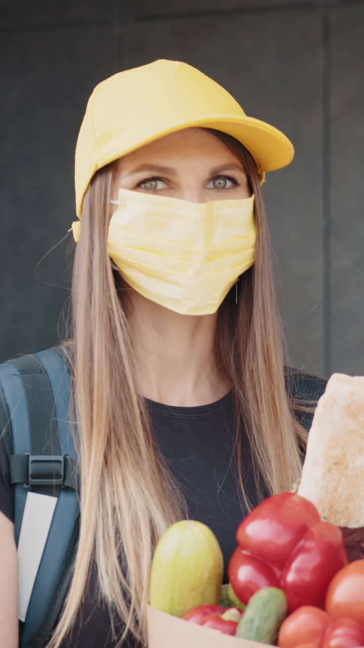 Delivery woman wearing a mask holding a grocery bag with fresh vegetables
