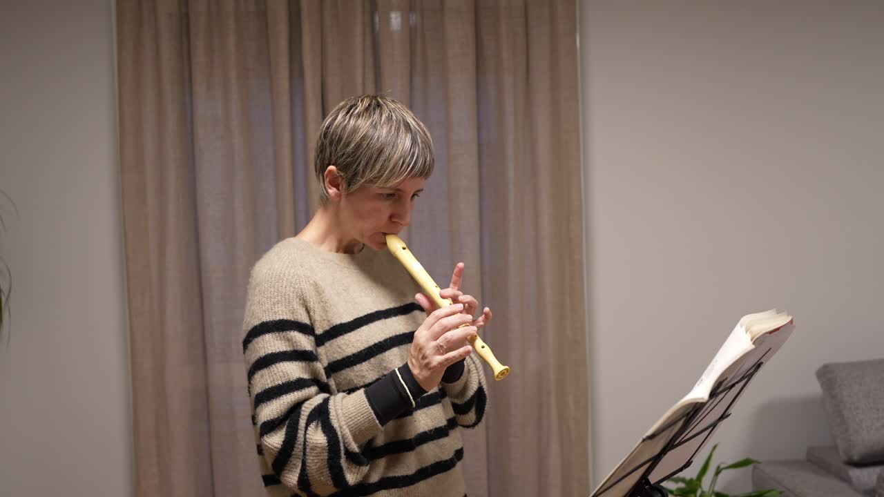 Donna che suona il flauto dolce e legge uno spartito musicale a casa