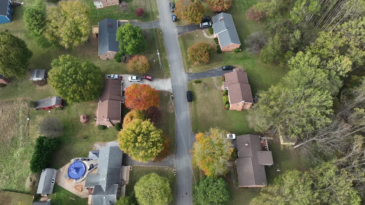 Aerial top down of houses along road between colored trees in autumn. Sunny day in America. Fall foliage in quiet suburbia. Middle class one family homes in different colors. New England, USA