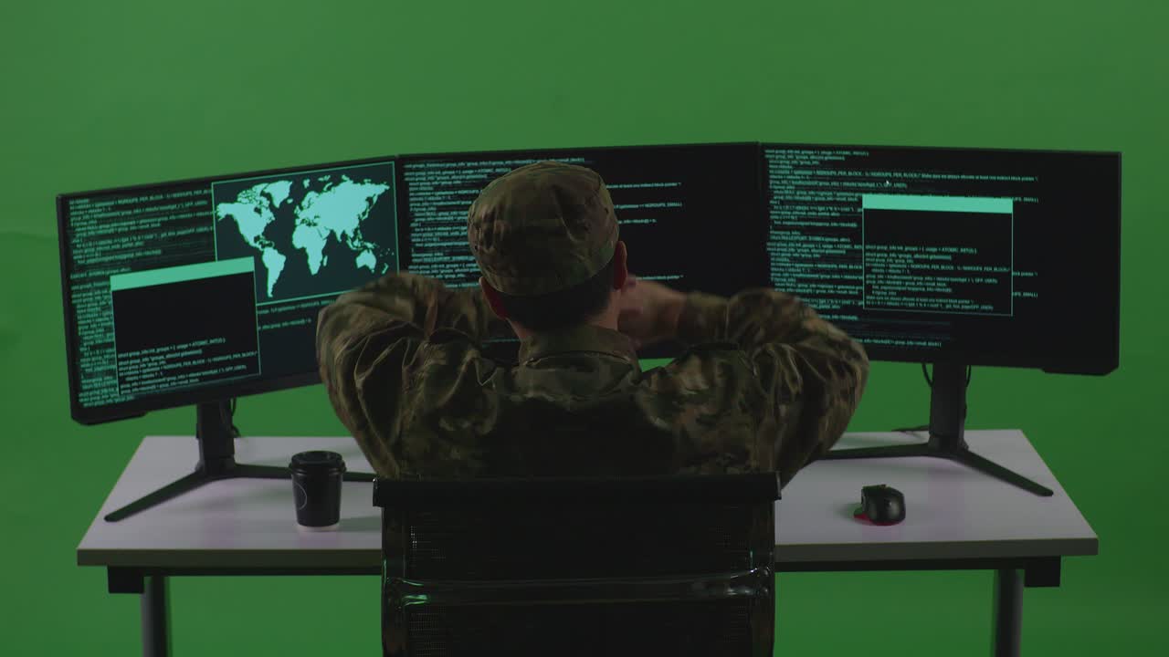 vista trasera de un cansado hombre asiático soldado desarrollador estirándose mientras escribe código con múltiples pantallas de computadora en el estudio de pantalla verde