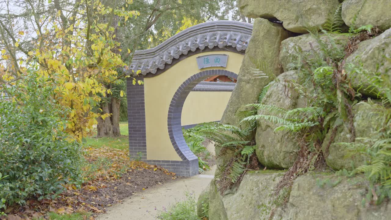 A traditional Chinese moon gate stands in a serene garden in Parc de Maurepas. The path leads through the circular entrance, surrounded by autumn trees, Rennes in France