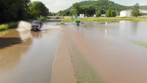 4k-Luftaufnahme-Eines-Lastwagens,-Der-Schnell-Durch-Hochwasser-Fährt-Und-über-Eine-Straße-Außerhalb-Einer-Kleinen-Stadt-Fährt