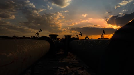 pipeline and working oil pump jacks in a against sunset extracting crude oil. pumping fossil oil is one of the methods of energy generation from renewable energy sources