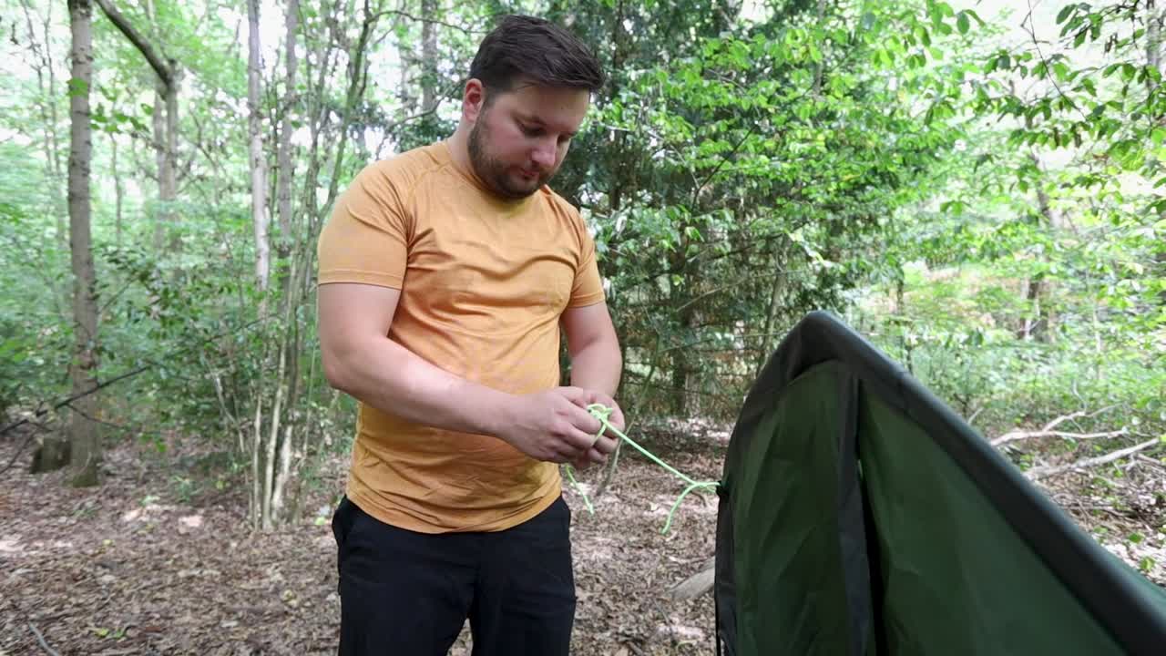 Angry man fails to untie a knot of a tent rope at a forest campsite