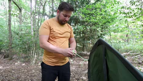 angry man fails to untie a knot of a tent rope at a forest campsite