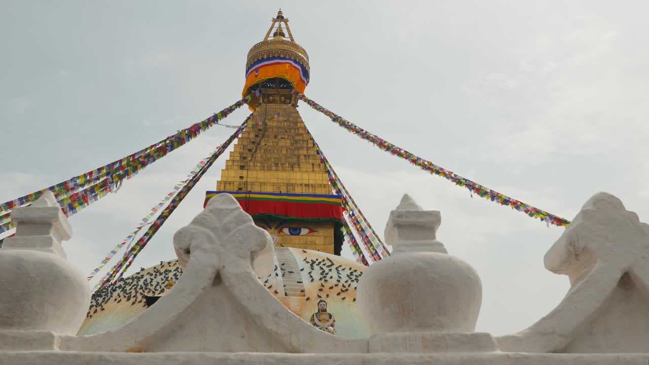 Panning clip looking upwards at elaborate golden temple in Kathmandu, Nepal, with white carved decorations in foreground